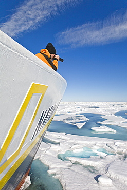 A photographer on the bow of the expedition travel ship National Geographic Endeavour photographing the ice leads in the Barents Sea, Norway.