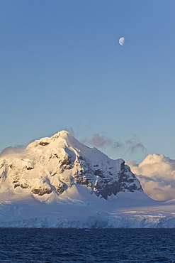 The Lindblad Expedition ship National Geographic Explorer in Dahlman Bay in late evening light as the waxing moon rises on the west side of the Antarctic Peninsula in Antarctica. 