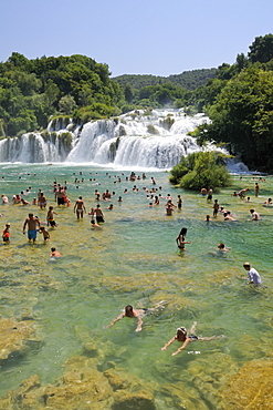 Tourists bathing in pools in the Krka river below Skradinski buk waterfalls, Krka National Park, Sibenik, Croatia.